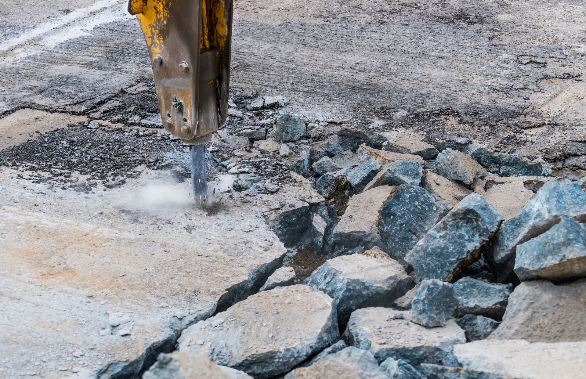 Close-up of demolition hammer with dust and sparks and broken concrete pieces